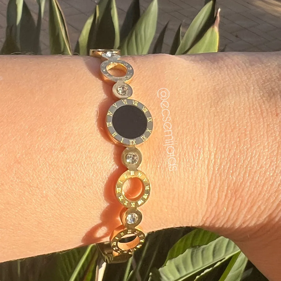 Bracelete com pedra redonda maior no centro com bordas com números gregos, zircônias redondas intercaladas com aros redondos vazados - aço dourado